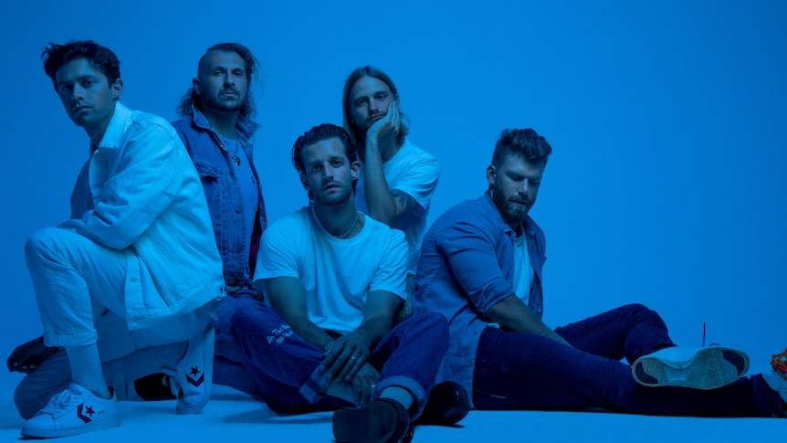 Press shot of The Rubens, band sitting on ground; shot against blue background