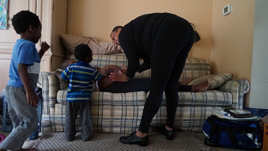 Midwife Claudia Booker places her hands on the stomach of expectant mother Binahkaye Joy, whose two toddlers join in.