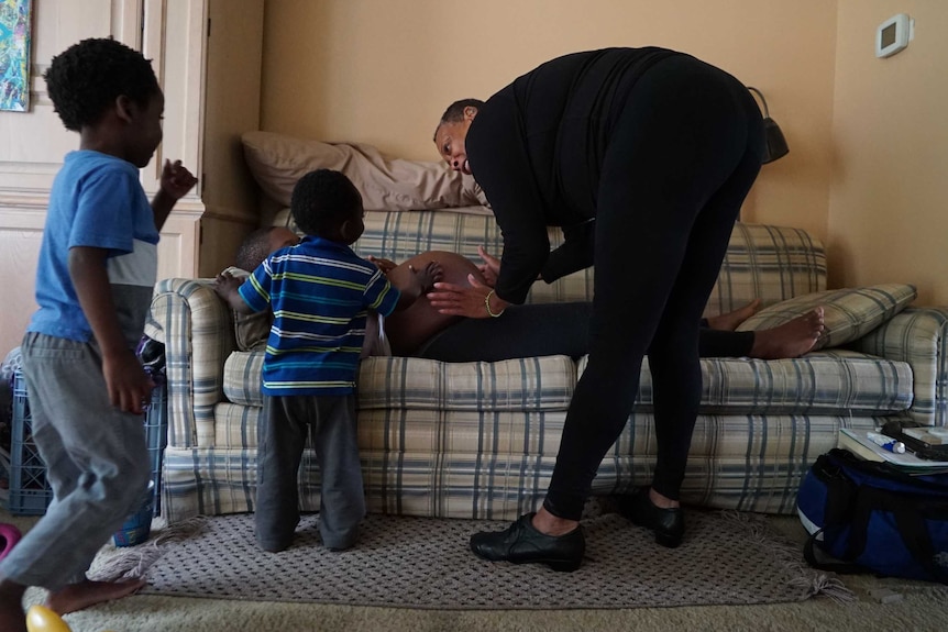 Midwife Claudia Booker places her hands on the stomach of expectant mother Binahkaye Joy, whose two toddlers join in.