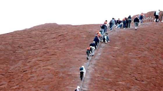 Climbers walk up a slope of Uluru
