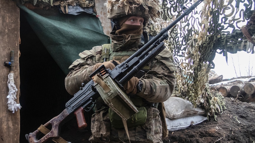 A soldier in camouflage stands with a machine gun.