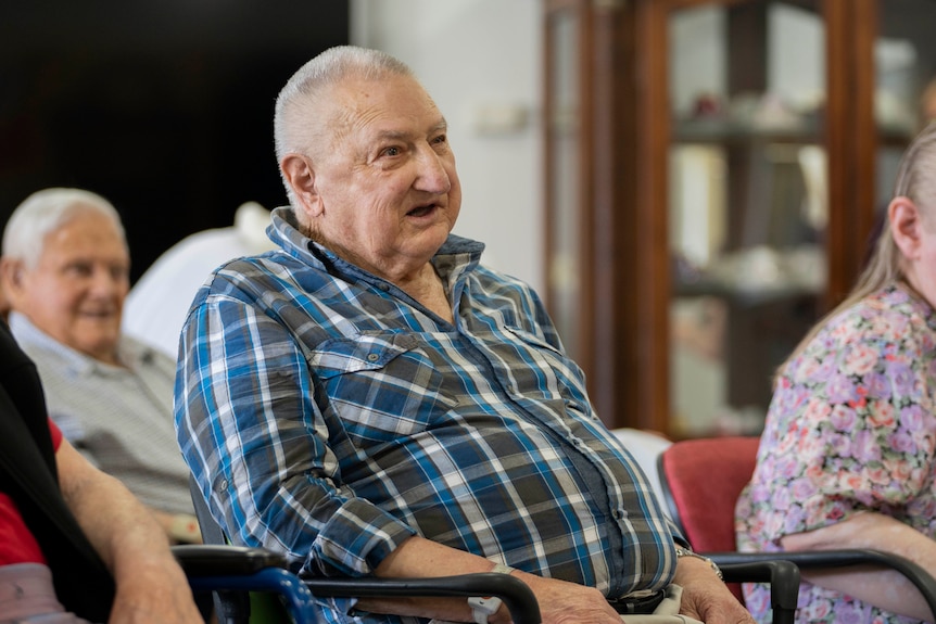 Male aged care resident in blue checkered shirt watching a performance.