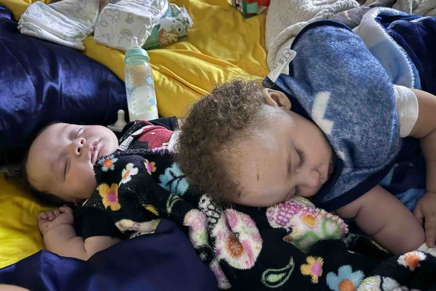 A baby and toddler sleeping among blankets