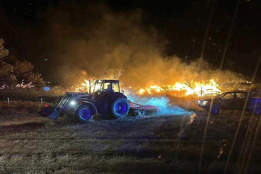 A farm trailer on a paddock on fire. 