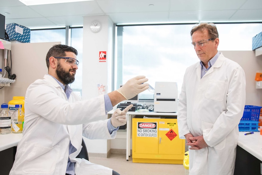 Professor Colin Pouton with Dr Harry Al-Wassiti are wearing white lab coats and working in a lab.