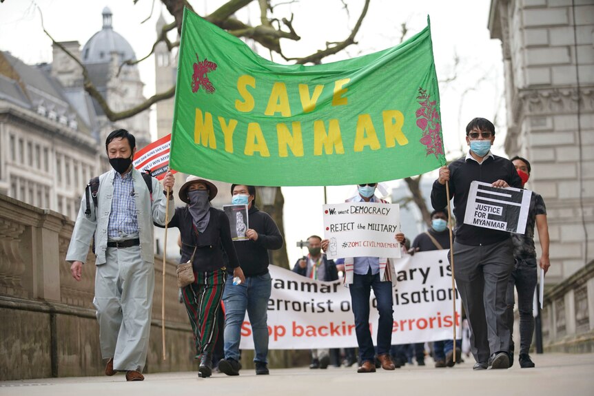 A small group of people walk the street holding a banner that says 'save myanmar'