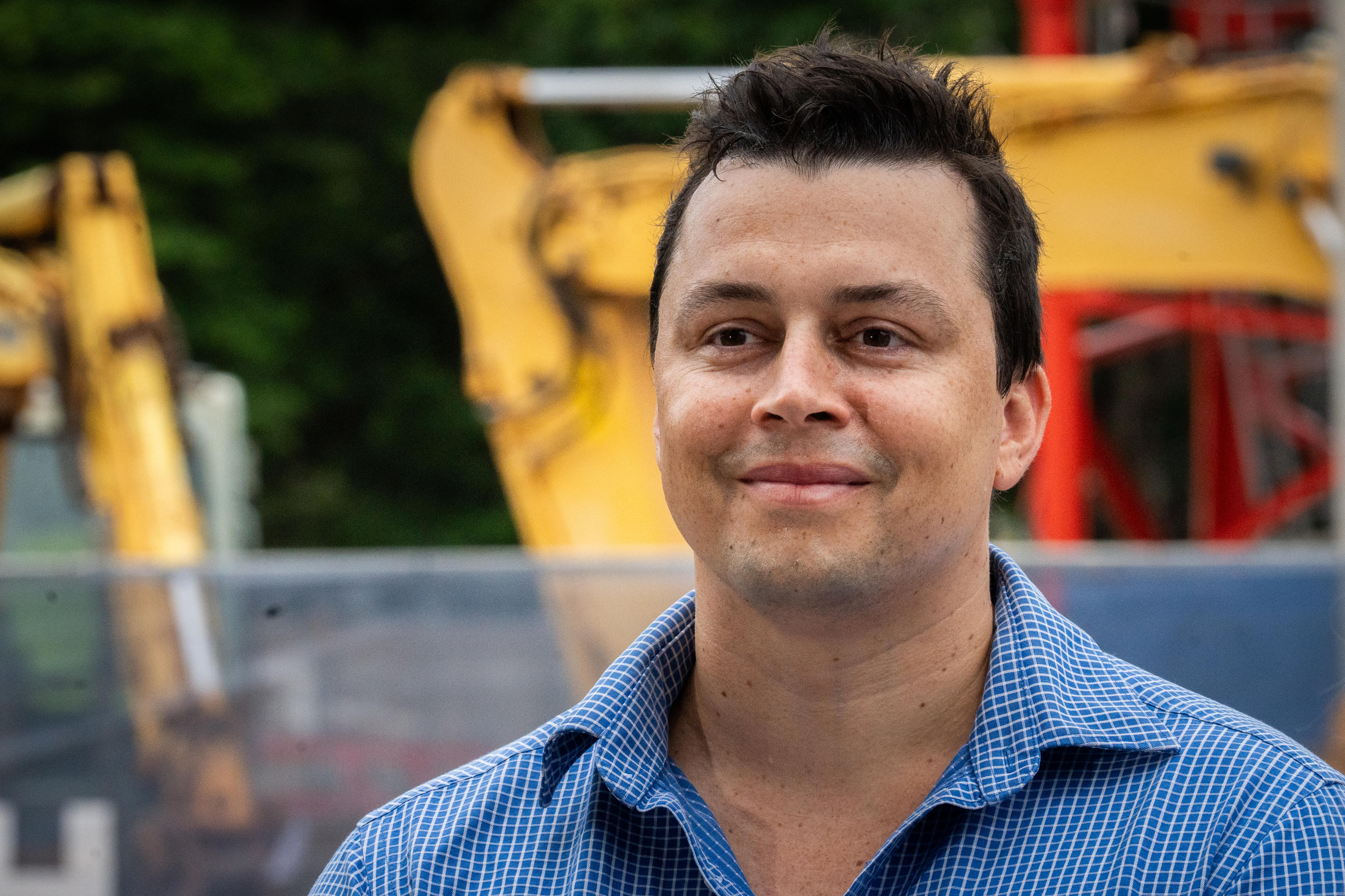 Um homem com cabelo curto e escuro parado perto de um canteiro de obras.