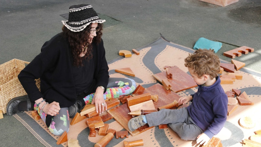 A woman and young boy playing with wooden blocks on a mat