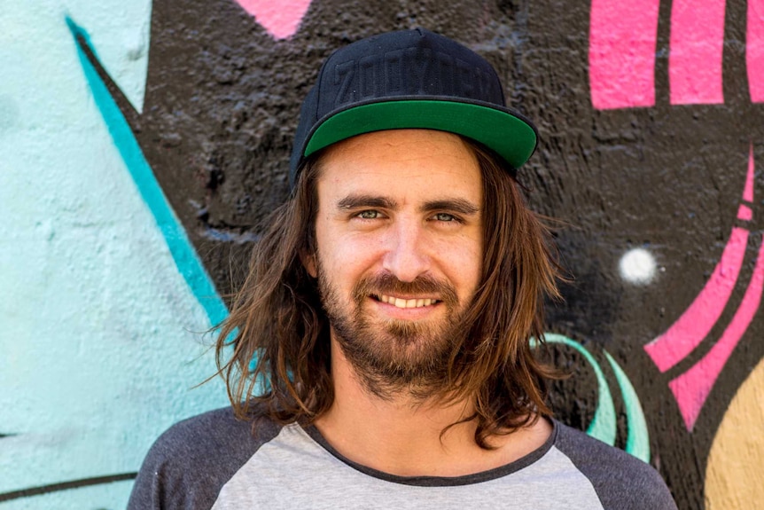 Shaun Hossack stands in front of a painting by Buttons, in Melbourne.