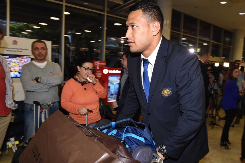 Israel Folau pushes his baggage through Sydney International Airport after returning from the Rugby World Cup.