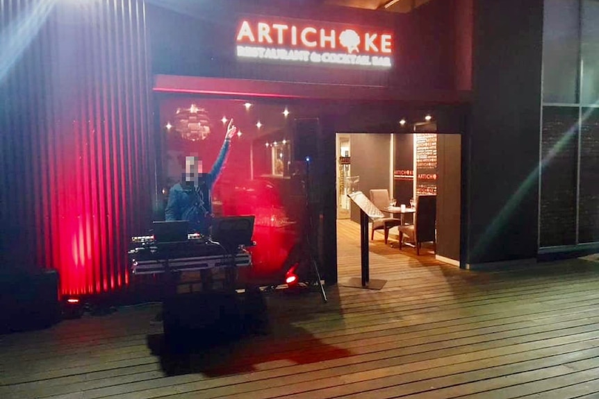 A DJ pointing a sign with the restaurant's name, Artichoke.