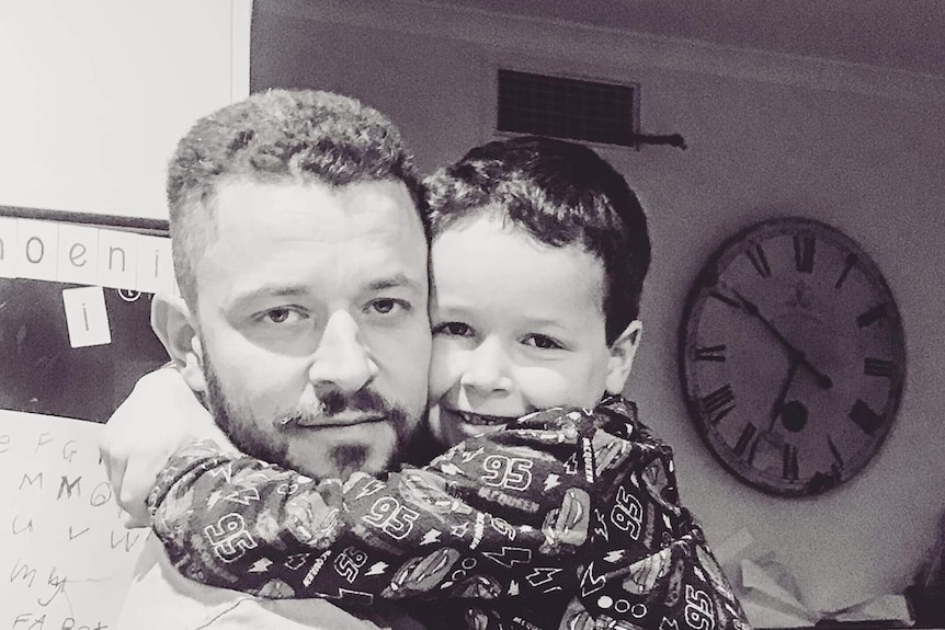 Canberra man Cliff Mapham holding his missing six-year-old son, Phoenix, with clock in background.