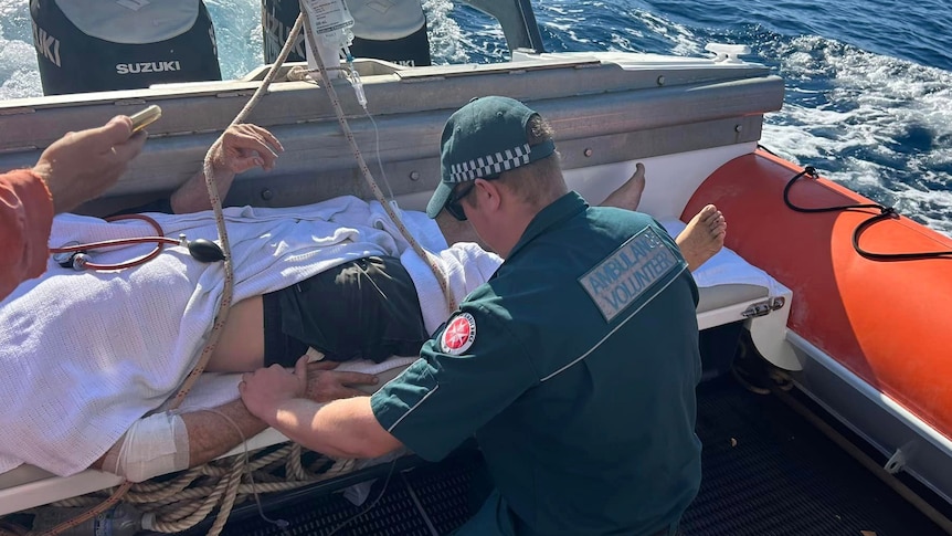 A man paramedic attends to a man on a stretcher onboard a boat