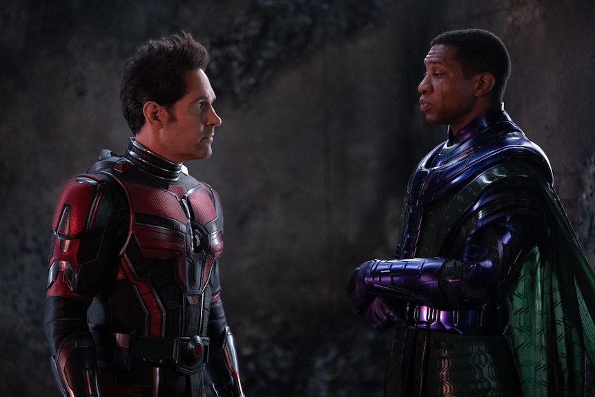 Two men in superhero costumes face each other looking serious.