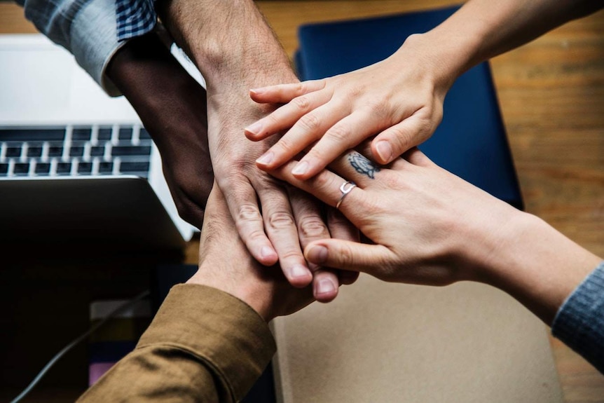 A group of people place their hands one on top of the other in a sign of teamwork.