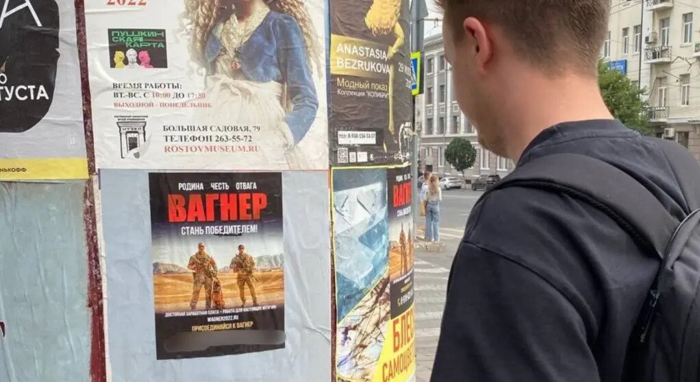 a man looks at a flyer taped to a poll, that feature two soldiers and a dog under big red Cyrillic letters