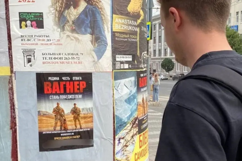 a man looks at a flyer taped to a poll, that feature two soldiers and a dog under big red Cyrillic letters