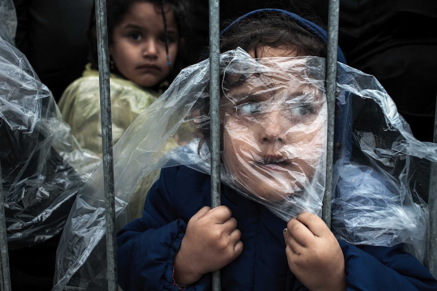 A child is covered with a raincoat while she waits in line to register at a refugee camp in Serbia.