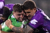 Two rival NRL players have their heads basically pressed together as one of them tackles the other