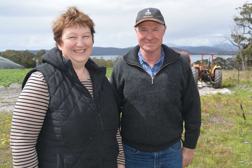 A smiling woman and man on a farm, wearing clothes for crisp weather.