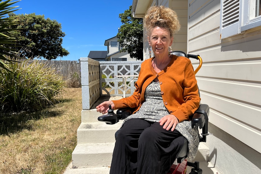 A woman sitting in a wheelchair in front of a house.