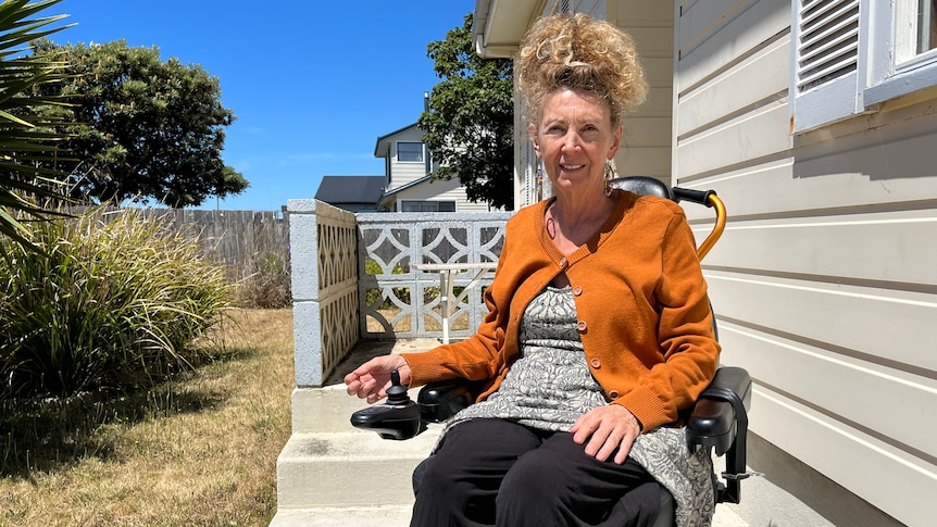 A woman sitting in a wheelchair in front of a house.