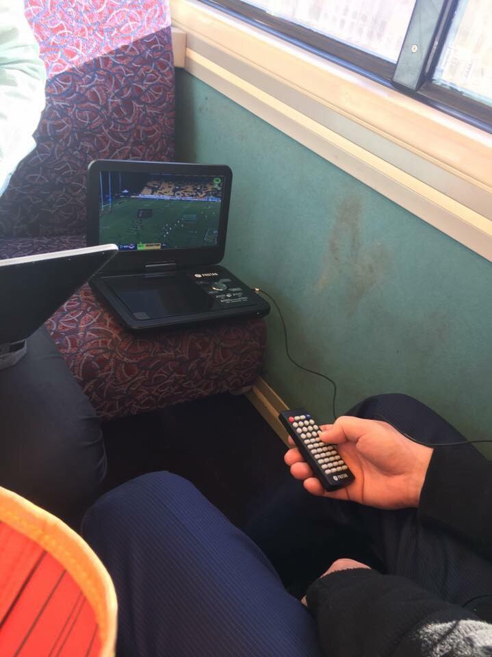 A portable DVD player takes up a space on a train. A man watches on with a remote in hand