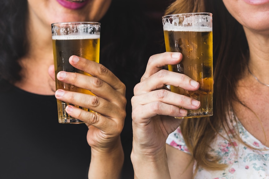 Two women hold up beers.