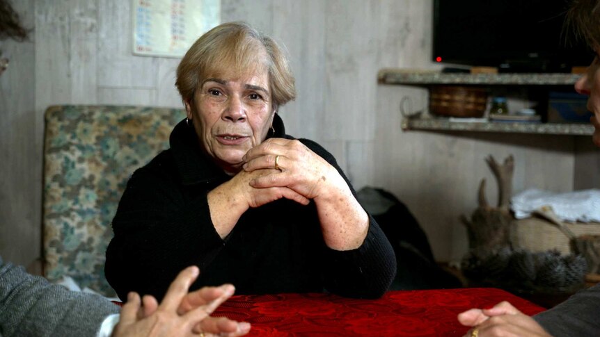 A woman wearing a black jumper looks at the camera while sitting at a table with two others.