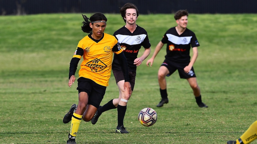 A player wearing a yellow soccer shirt dribbles the ball down a field.