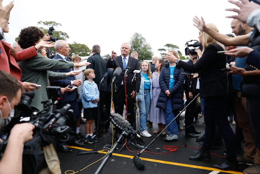 A wide angle of a journalists trying to get a question in, Morrison centre frame pointing.