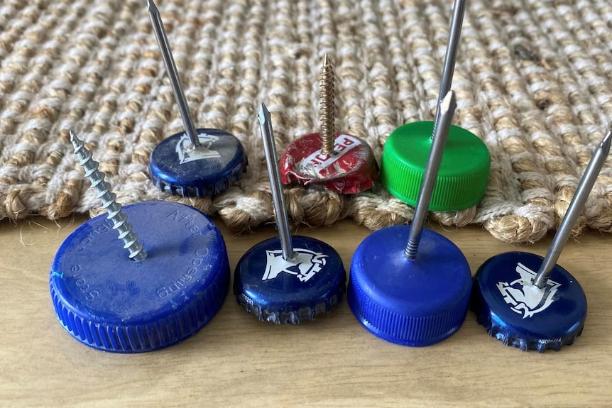 Bottle caps of varying sizes with nails in them. 