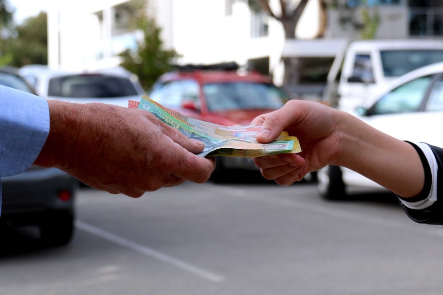 The hand of a young woman takes cash from the hand of an older man.