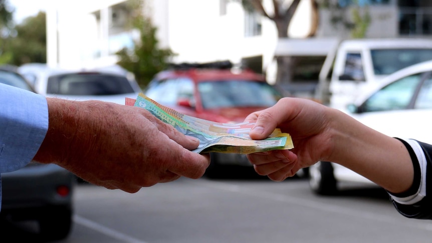 The hand of an older man takes cash from the hand of a young woman