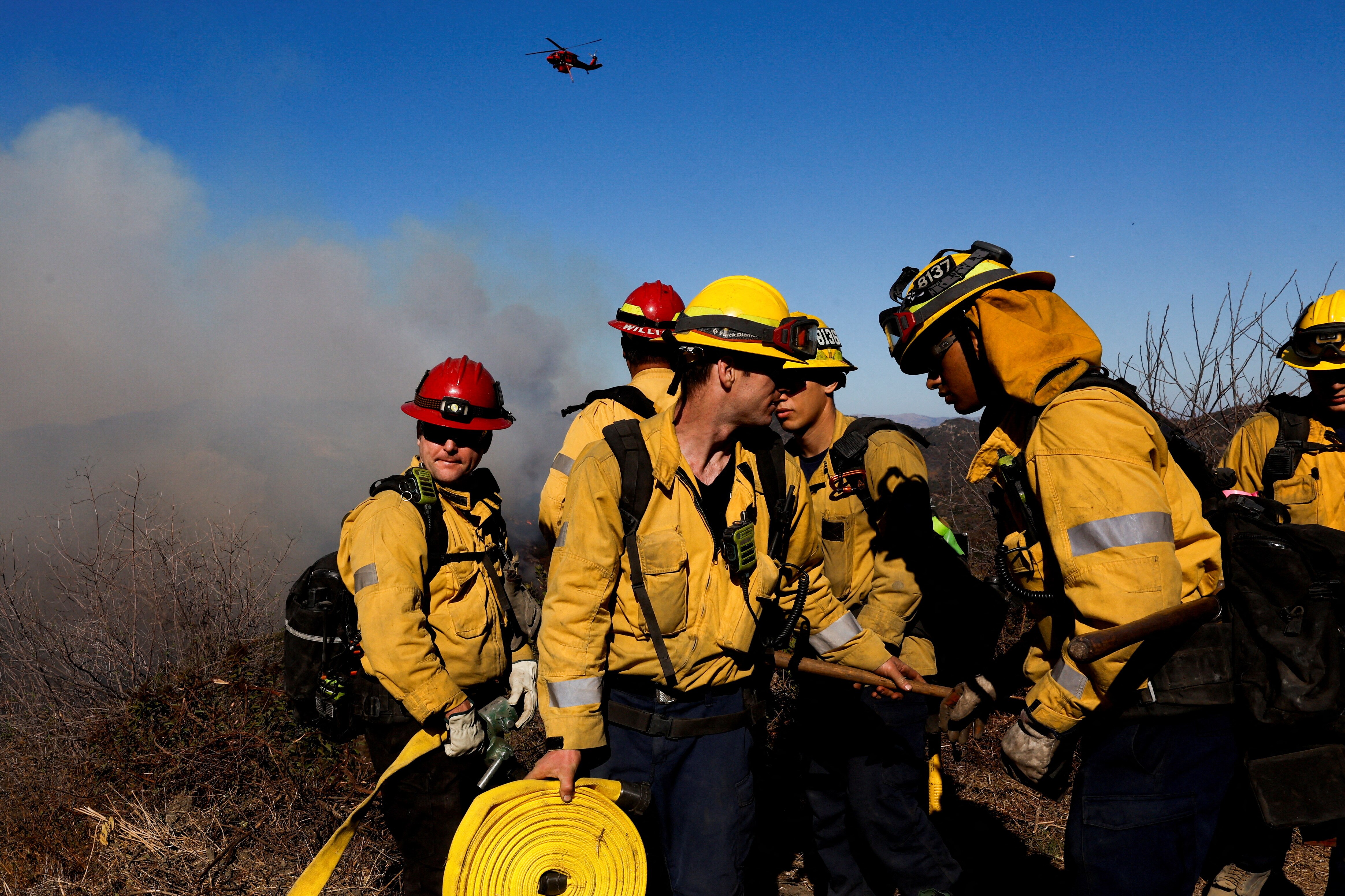 Firefighters gather near smoke in LA while an helicopter flies above