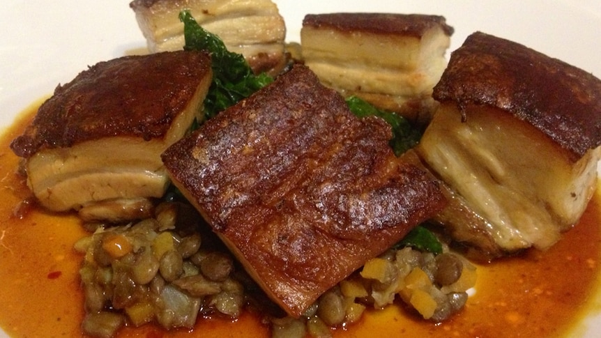 A close-up of cooked pork belly pieces on lentils.