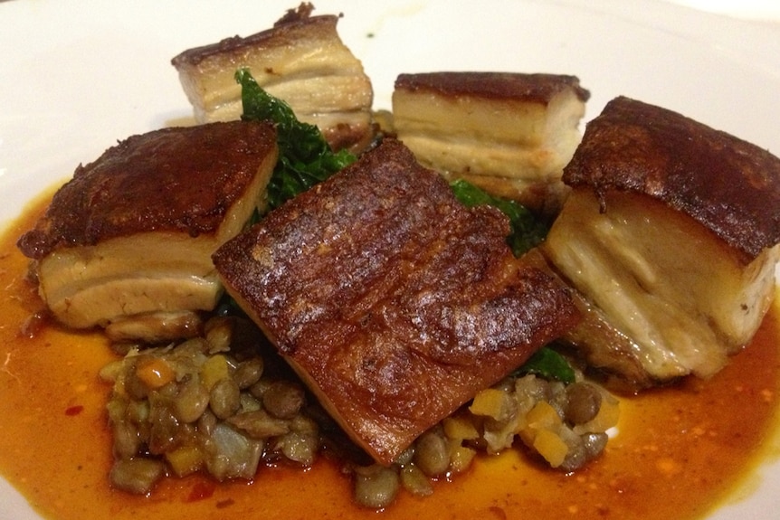 A close-up of cooked pork belly pieces on lentils.