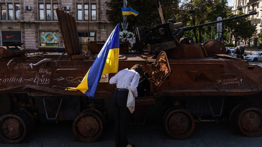 A woman holds the flag of Ukraine while looking into one of the destroyed Russian military vehicles.
