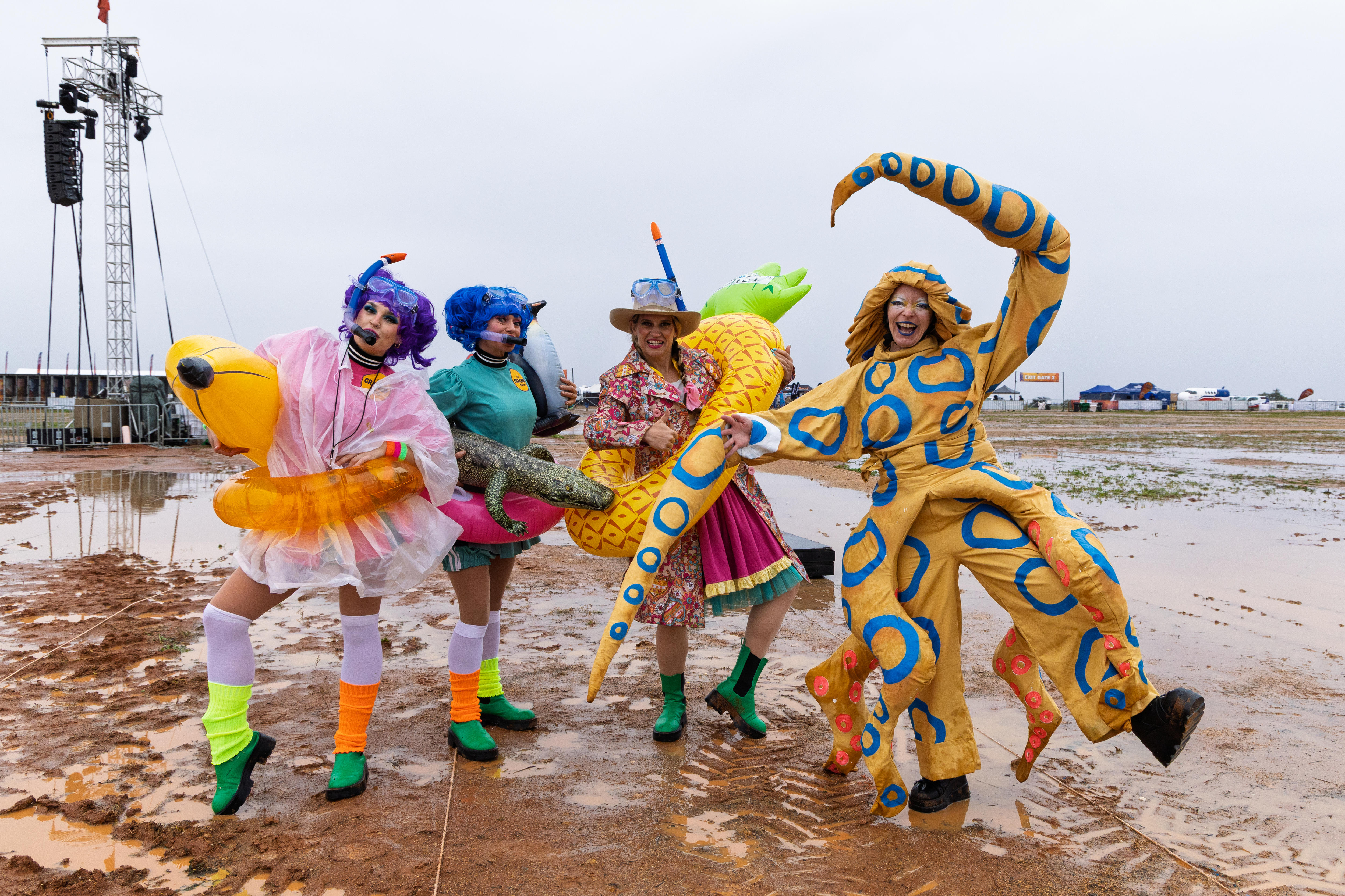 Four people in fancy dress stand in large muddle at an outback music festival