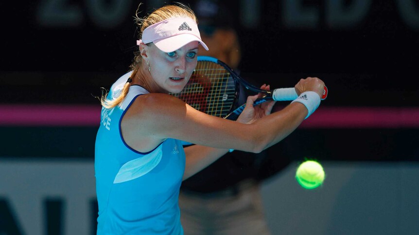 A female tennis player watches the ball intently as she hits a backhand return.
