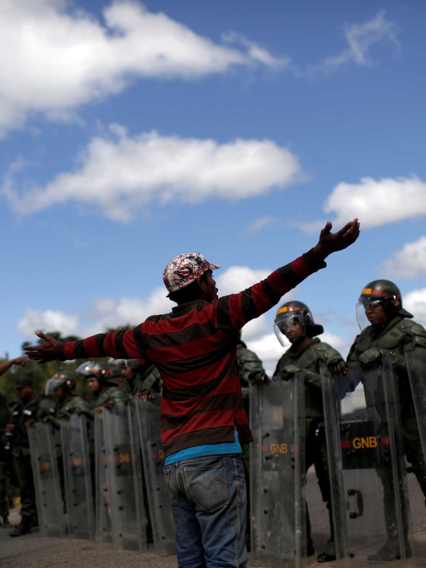 Men gesture at a row of soldiers wearing riot gear who are blocking the Venezuelan border.