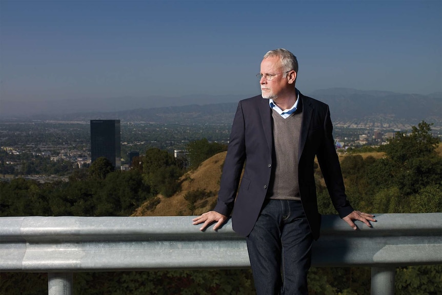 The novelist Michael Connelly standing in front of metal fence, LA in the background