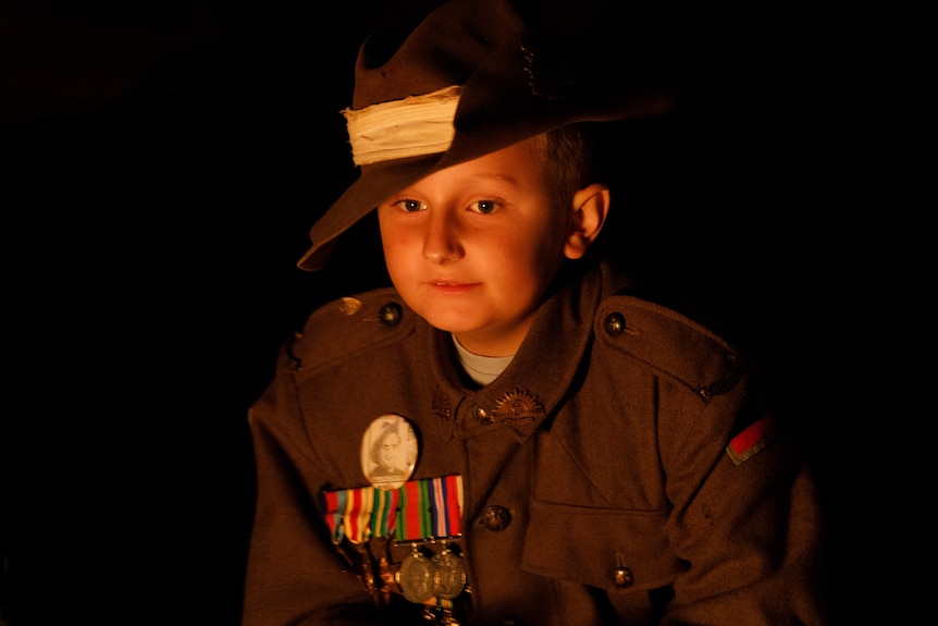 A boy in a large military uniform, with slouch hat and medals.