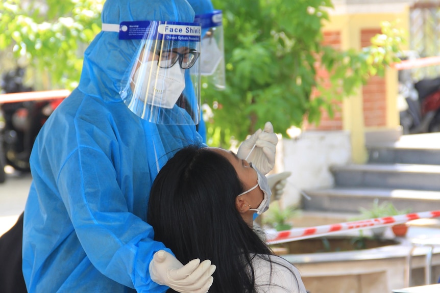 A girl is getting a nasal swab by another person in protective gear