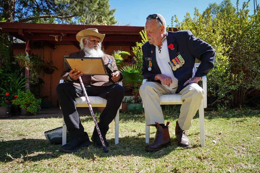 Two old men sit on chairs on a sunny day
