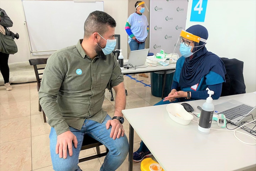 A man rolling his sleeve while talking to a health workers with a face shield