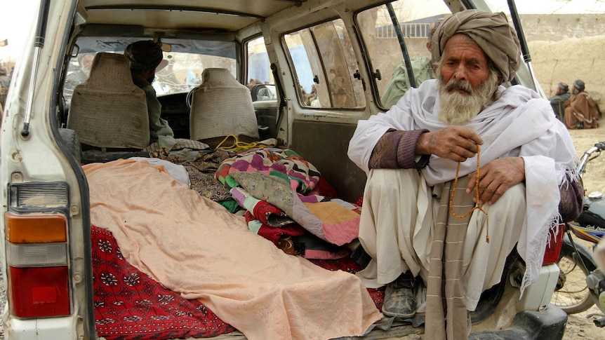 An elderly Afghan man sits next to the covered bodies of people who were killed by coalition forces in Kandahar