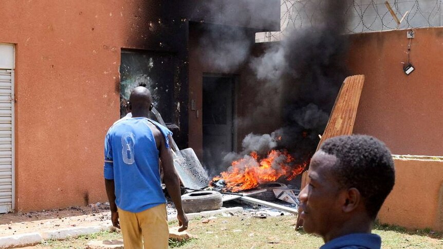 Man in blue shirt stands in front of burning door 