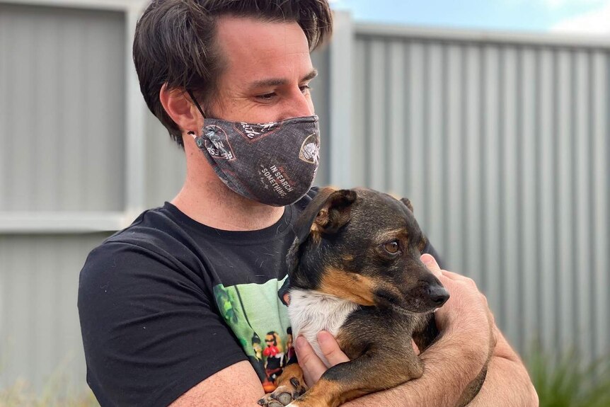 Man wearing facemask hugs small dog