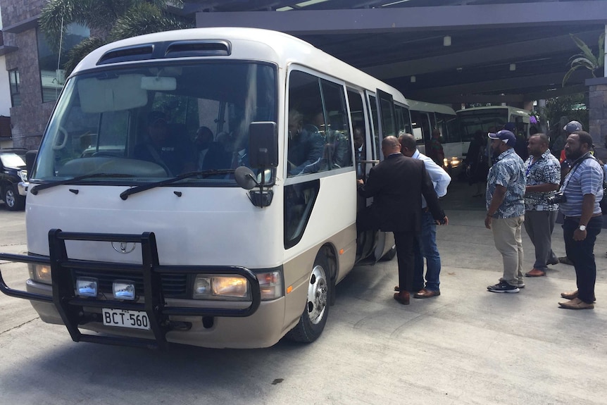 Men wait in line to board a white bus.